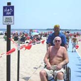 Parks Employee escorts man in wheelchair on beach mat