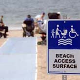 Sign on beach next to beach mat reads Beach Access Surface