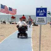 Man in wheelchair on beach mat next to sign reading Beach Access Path