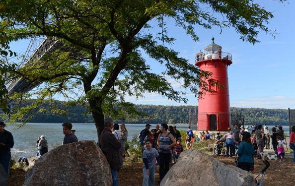 guests visit and hang around a little red lighthouse under a bridge at the water's edge