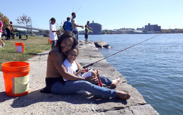 a woman and a child pose for a photo while fishing at the waterfront at Randall's Island